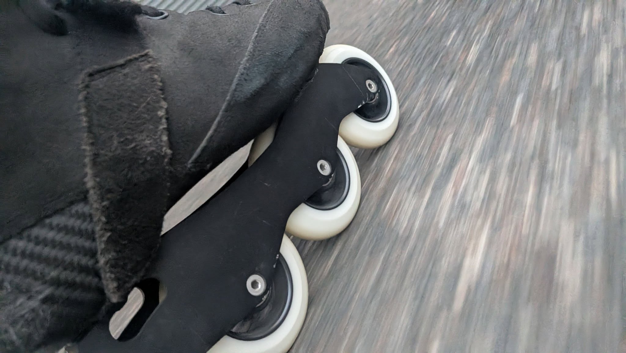 Close-up of white inline skate wheels rolling over a textured path